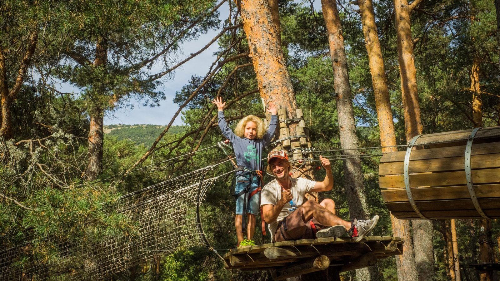 Père et enfant harnachés et casqués sur une plateforme perchée en forêt de pins, parcours accrobranche en famille près de Bordeaux