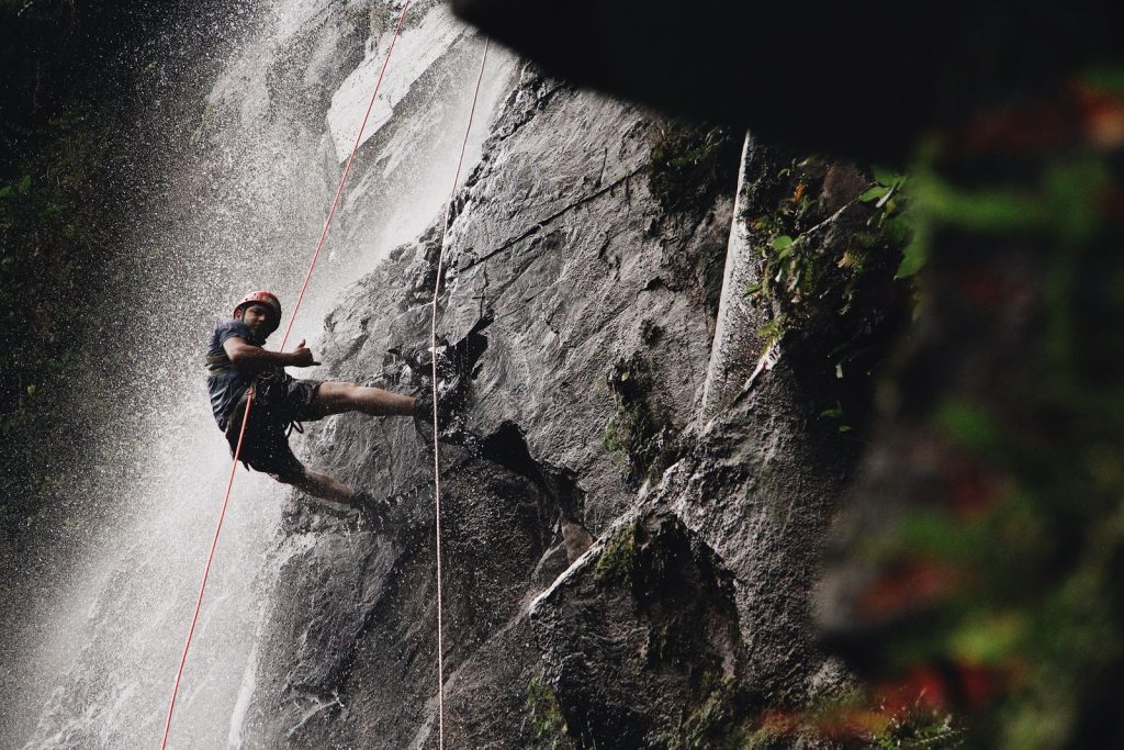 Canyoniste en rappel sur une paroi rocheuse sombre entre deux cordes, végétation dense en contrebas, canyoning dans les Pyrénées