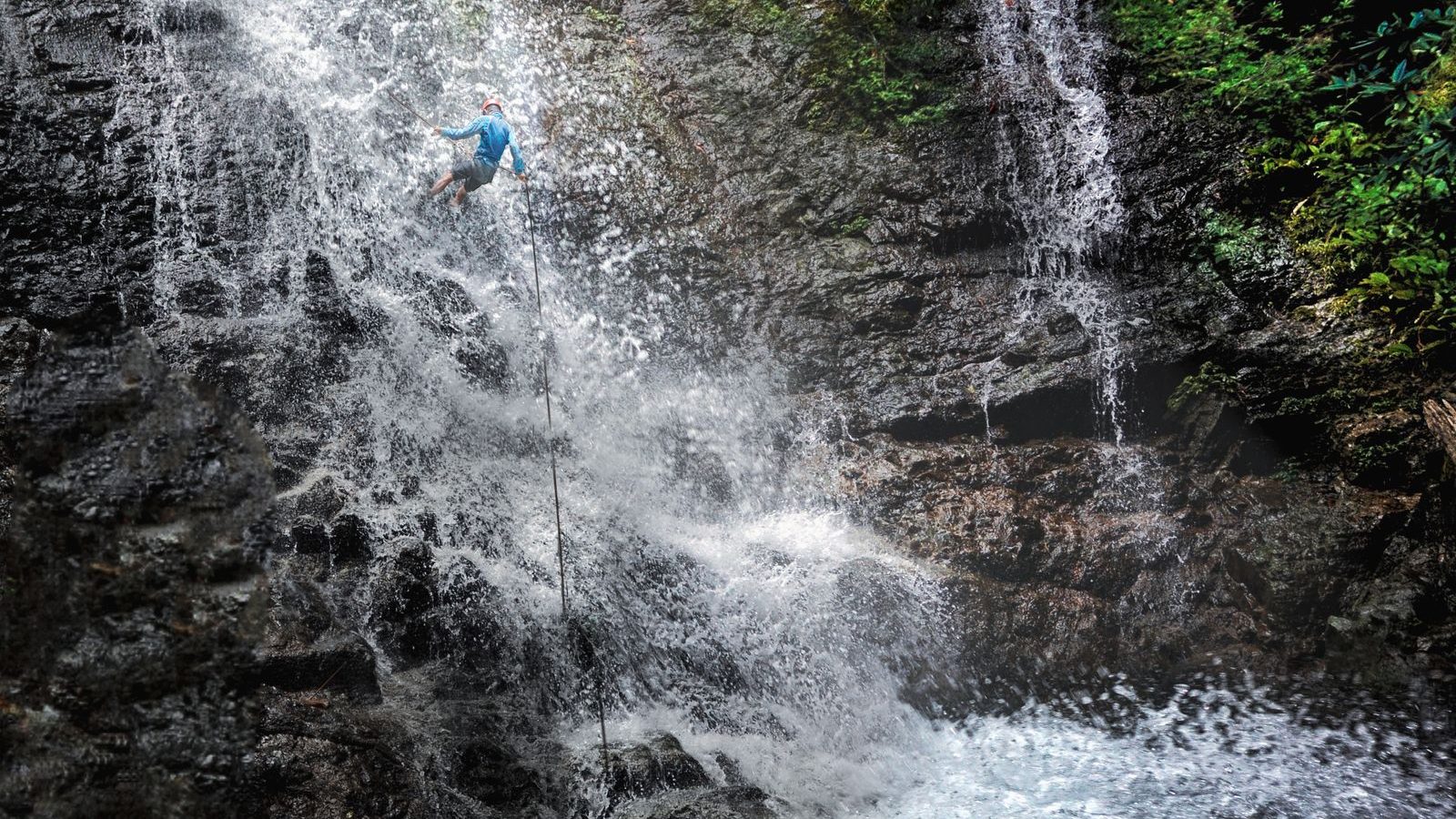 Canyoniste en rappel au milieu d'une cascade encaissée dans une gorge verdoyante, activité canyoning dans les Pyrénées