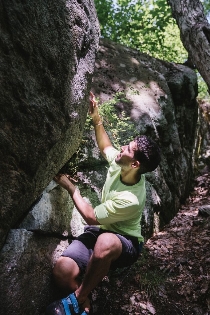 Grimpeur en chaussons d'escalade sur un bloc de grès en forêt, activité escalade à Fontainebleau