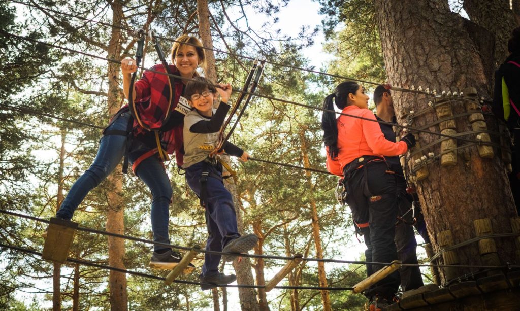 Mère et enfant harnachés sur un pont de câbles suspendu en forêt, parcours accrobranche en famille à Lyon