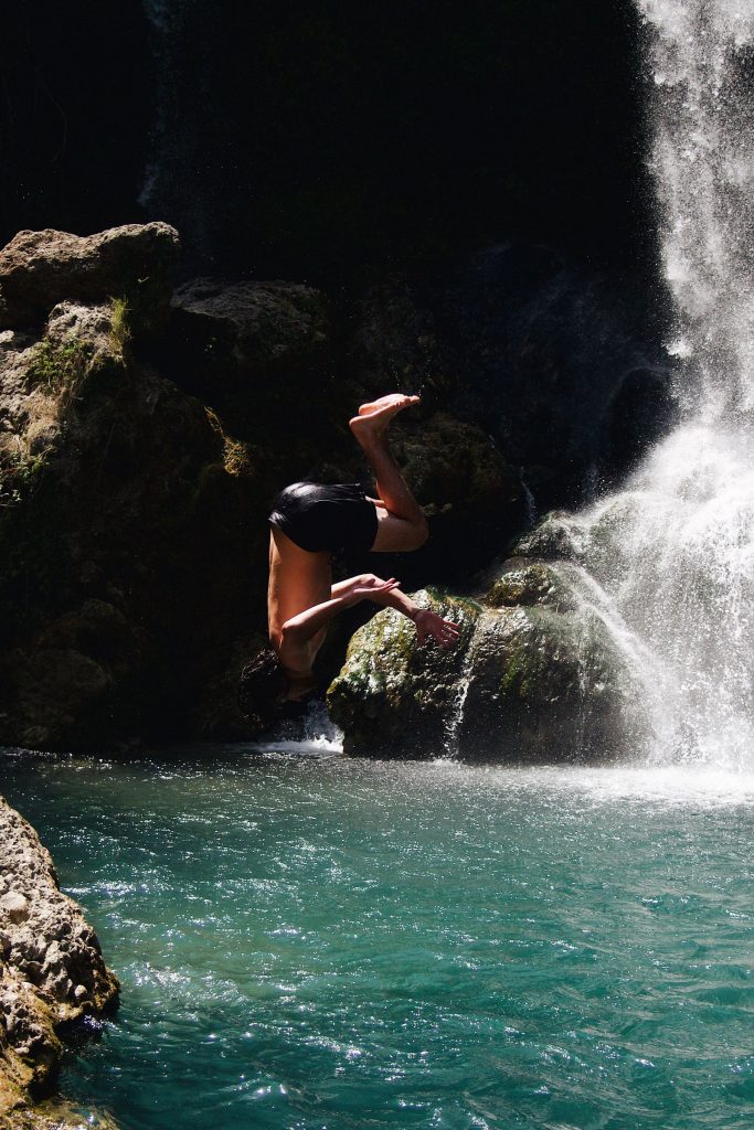 Canyoniste sautant d'une paroi rocheuse dans une vasque au pied d'une cascade, activité canyoning dans les Alpes-Maritimes