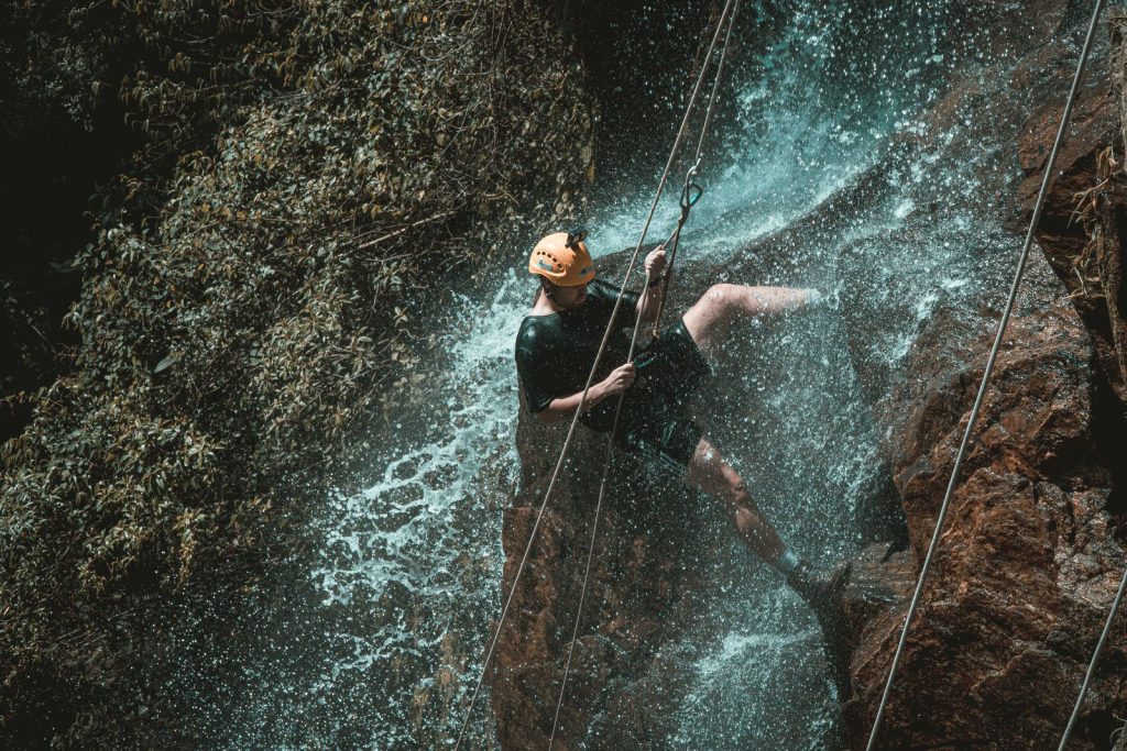 Canyoniste casqué en rappel sous les embruns d'une cascade, corde rouge tendue sur la paroi rocheuse, activité canyoning près d'Annecy