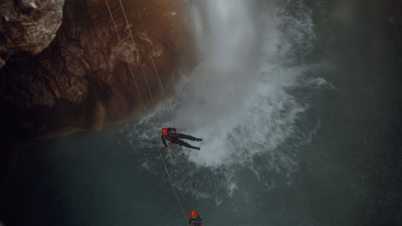Deux canyonistes casqués en rappel au-dessus d'une vasque au pied d'une cascade dans un canyon encaissé, illustration du canyoning près d'Annecy