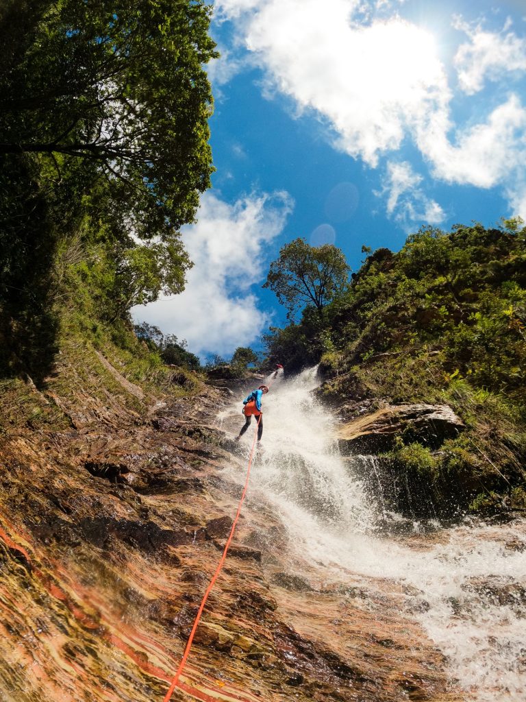 Canyoniste en descente encordée au milieu d'une cascade sous un grand soleil, gorges calcaires, canyoning en Ardèche
