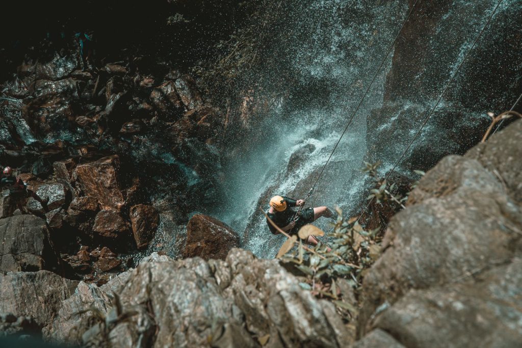 Canyoniste casqué en rappel sous une cascade dans un canyon aux roches chaudes, illustration du canyoning en Corse