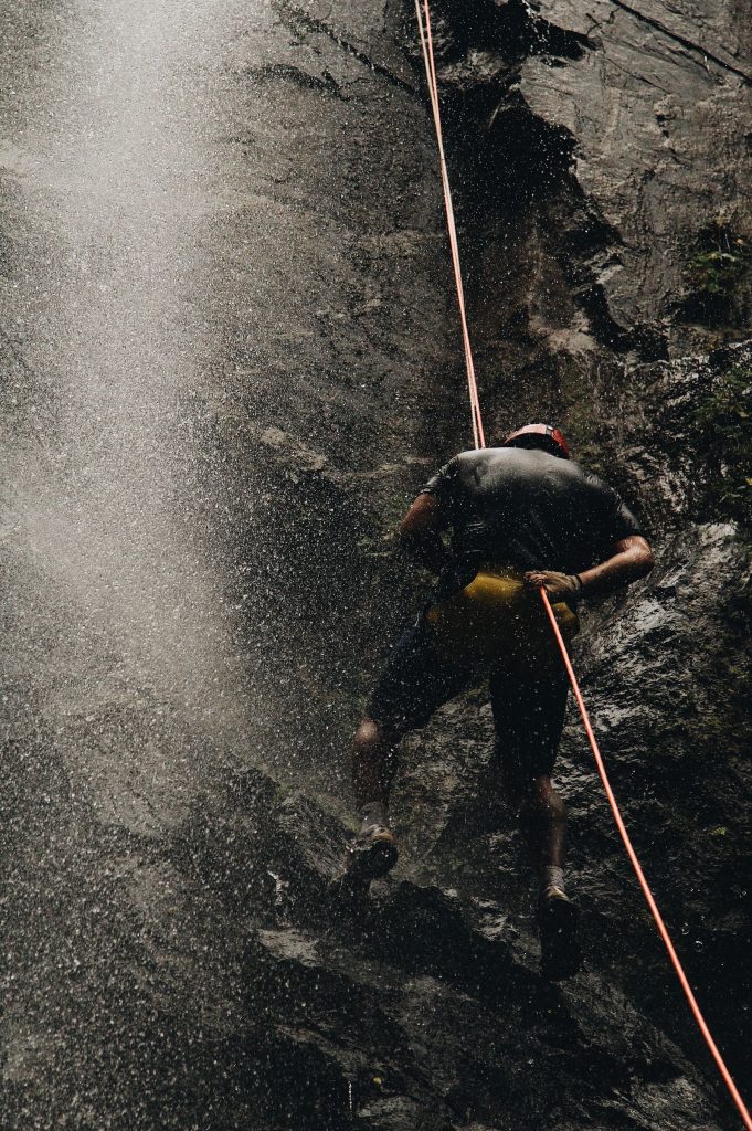 Canyoniste casqué en rappel au pied d'une cascade sombre et encaissée, activité canyoning dans l'Hérault