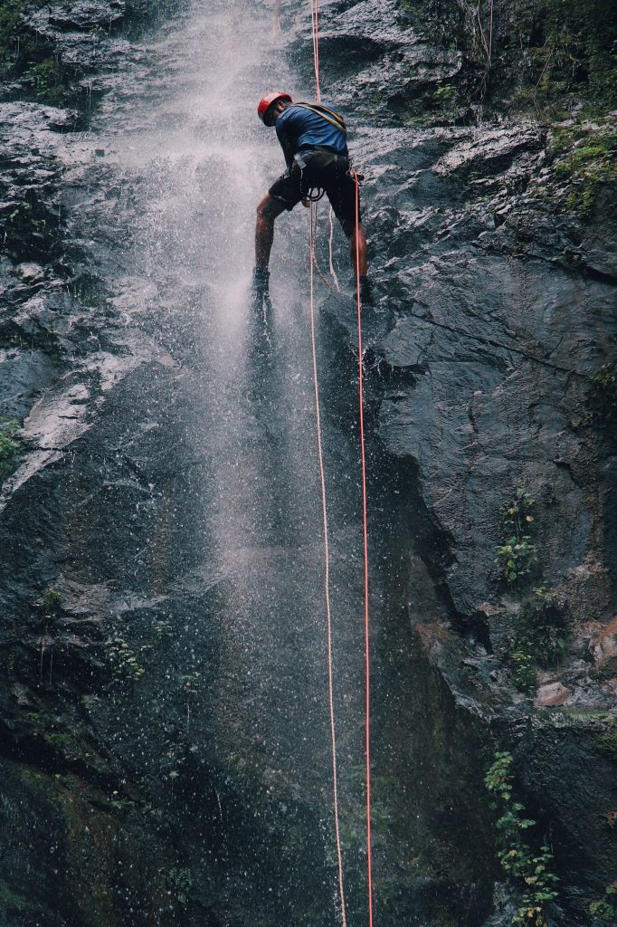 Canyoniste casqué en rappel encordé sous une cascade, illustration des formules et tarifs de canyoning