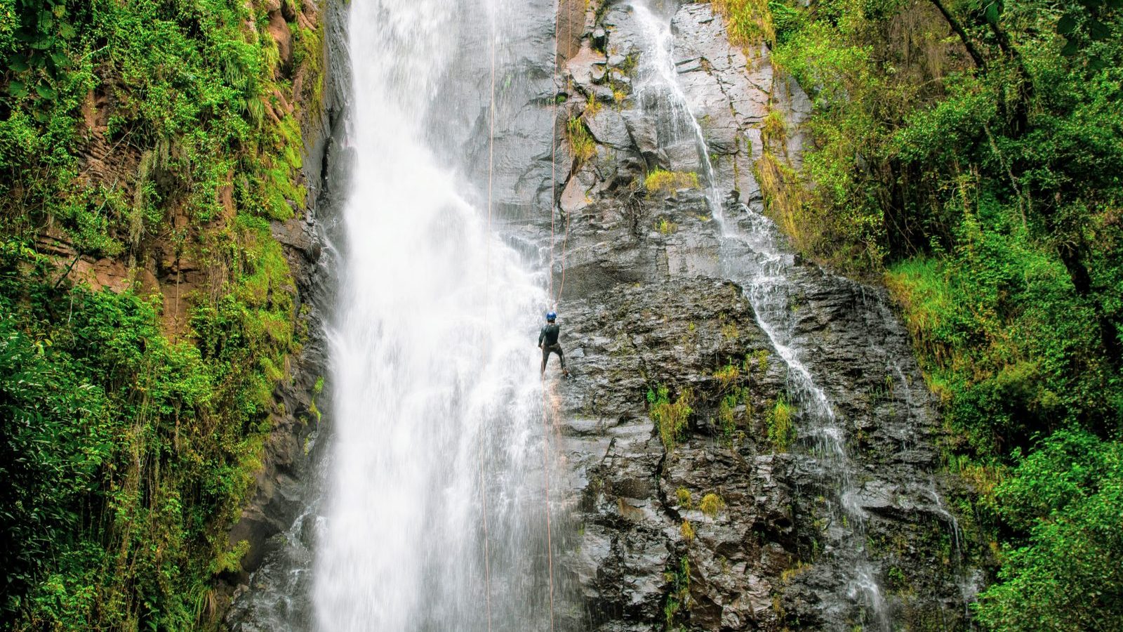 Pratiquant de canyoning en rappel devant une cascade encaissee