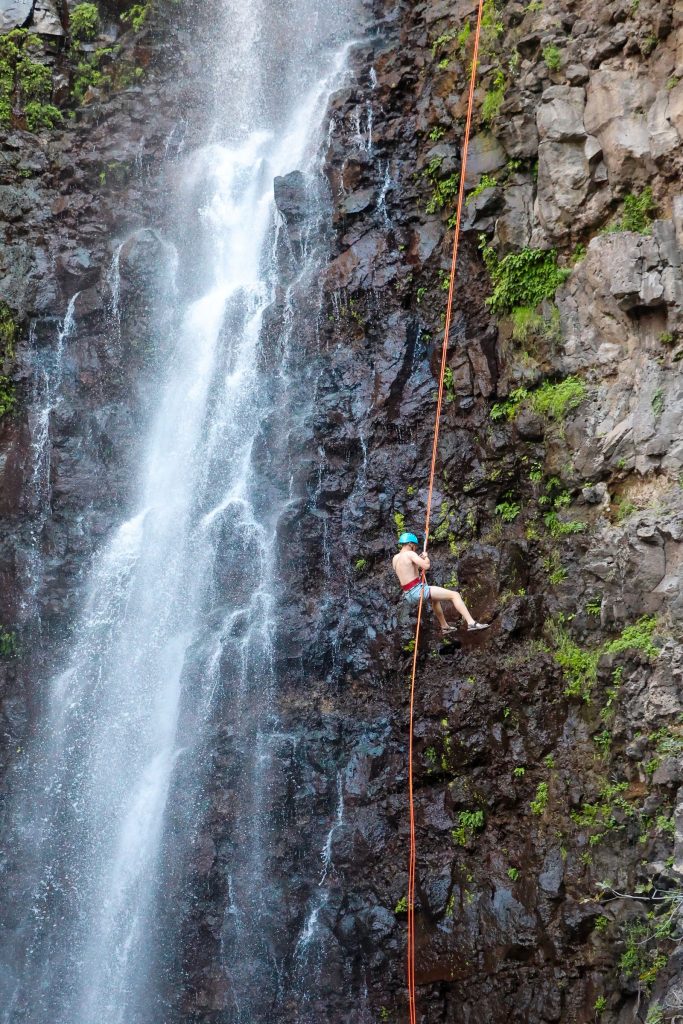 Canyoniste en rappel le long d'une paroi rocheuse moussue au pied d'une cascade, activité canyoning dans les Vosges