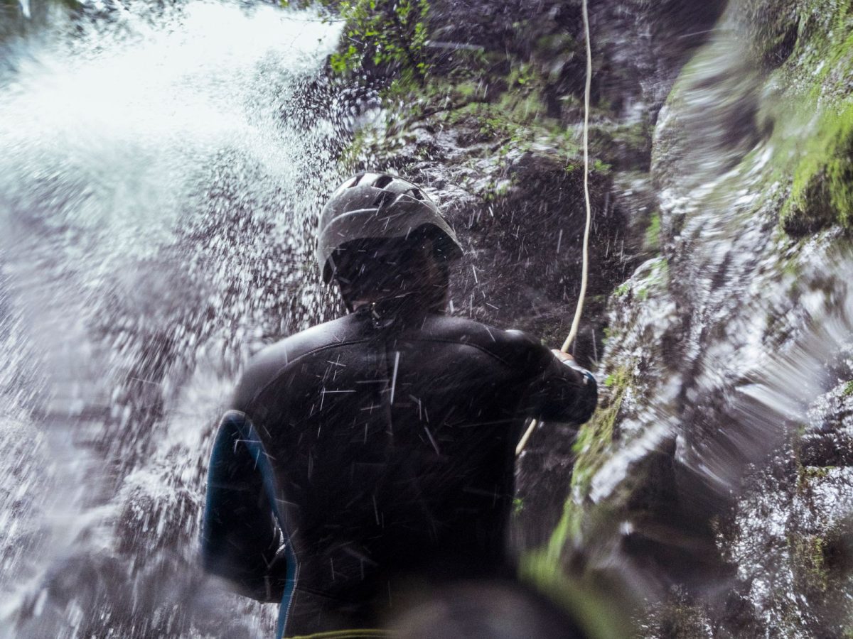 Canyoniste en rappel sous les embruns d'une cascade encaissée en forêt, activité canyoning dans les Vosges