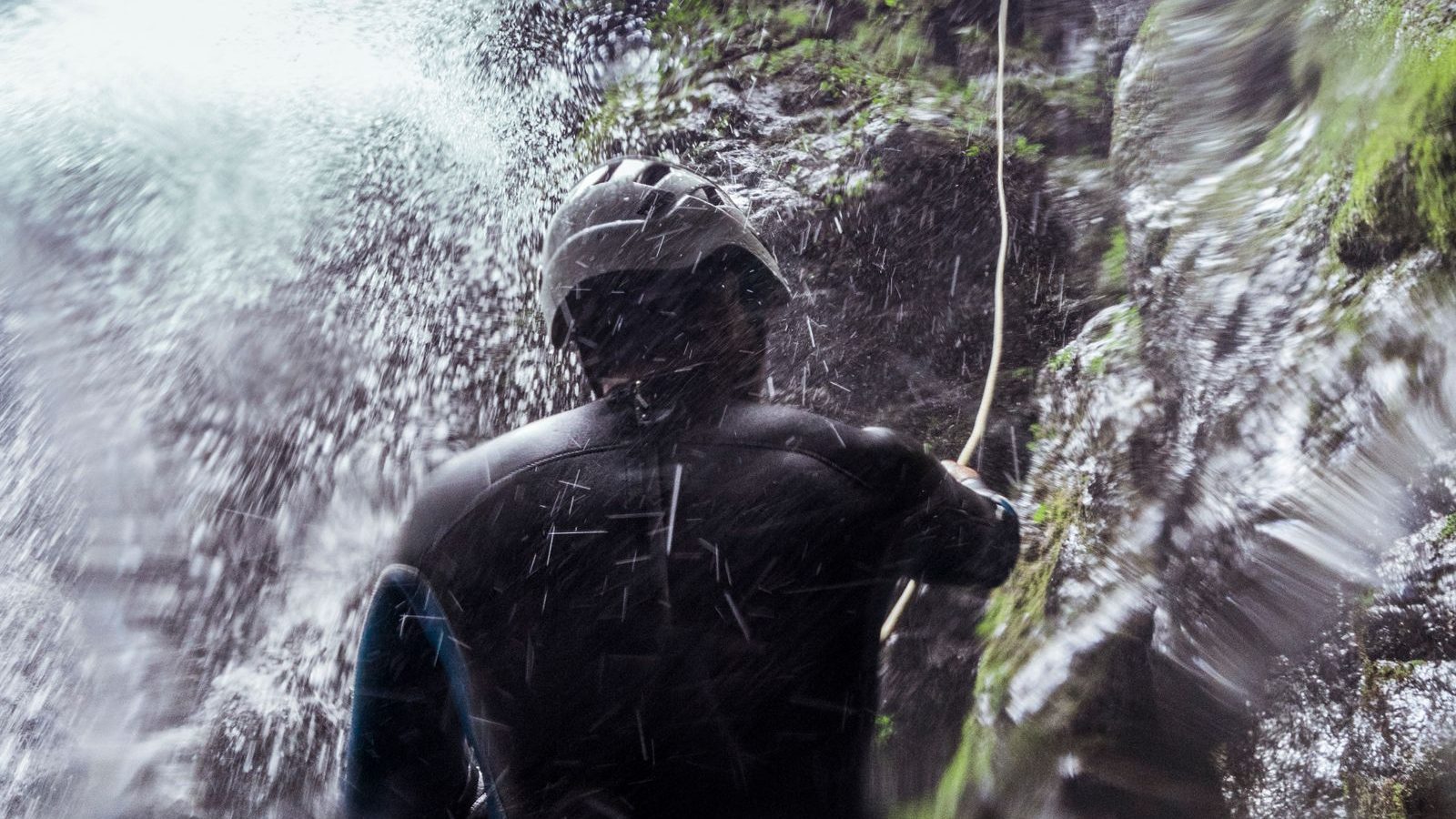 Canyoniste en rappel sous les embruns d'une cascade encaissée en forêt, activité canyoning dans les Vosges