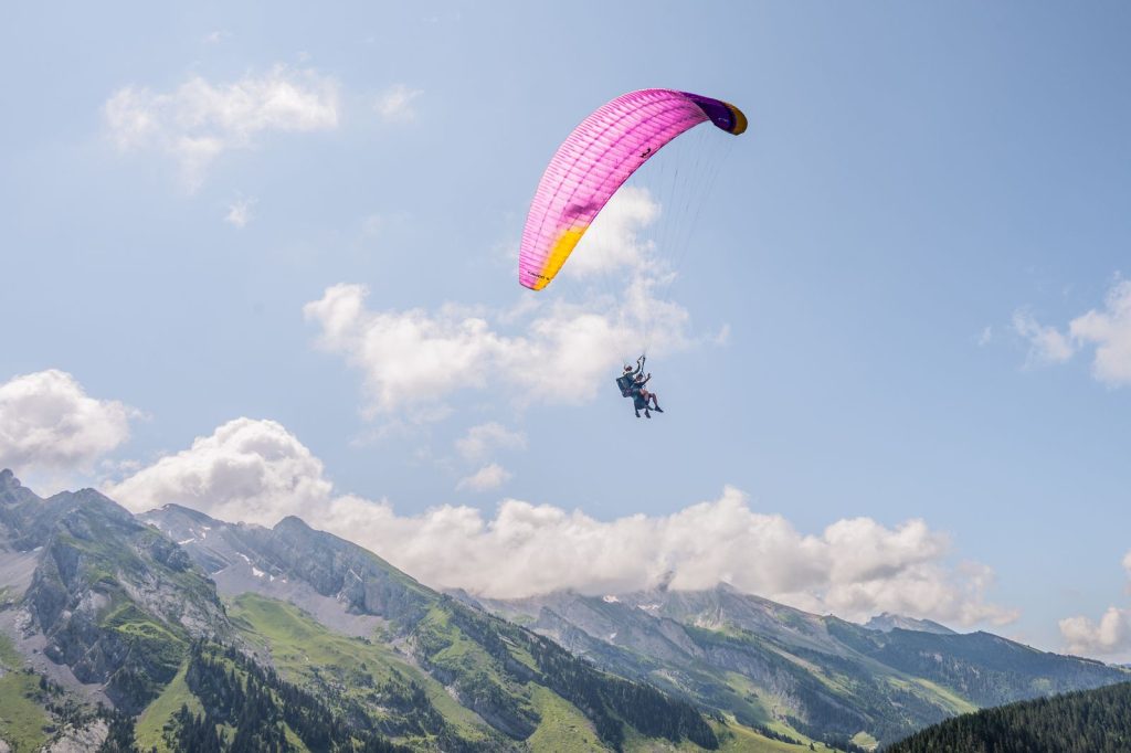 Voile de parapente biplace en vol au-dessus d'une chaîne de montagnes alpines verdoyantes, pilote et passager visibles