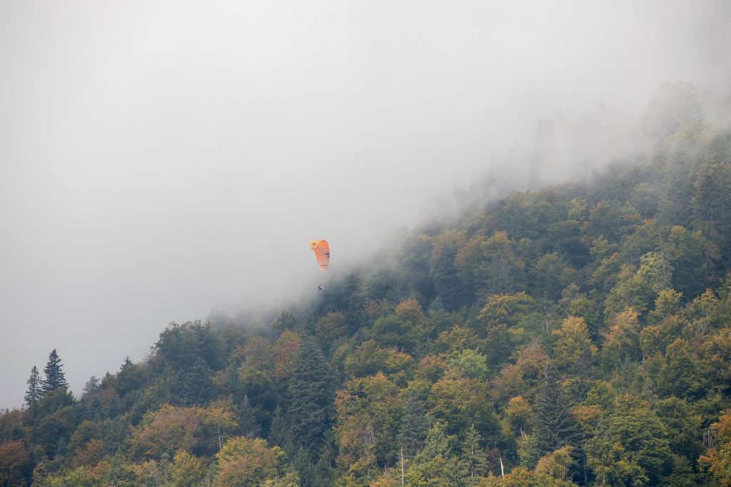 Parapente survolant un versant forestier aux couleurs d'automne partiellement pris dans la brume, illustration du parapente dans les Pyrénées