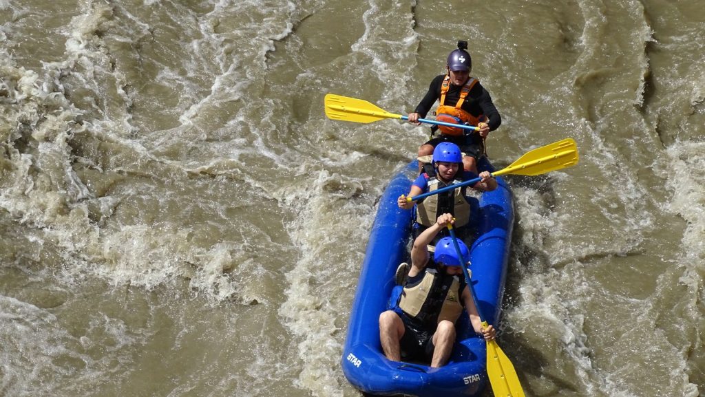 Vue plongeante sur un raft bleu et son équipage pagayant dans une rivière aux eaux vives et troubles, rafting en Ardèche
