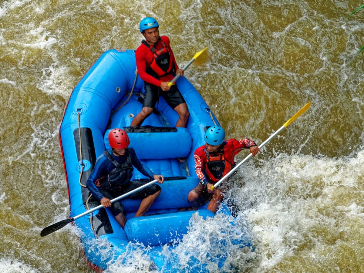 Trois rafteurs casqués pagayant dans un raft gonflable au milieu des rapides, activité rafting en eaux vives