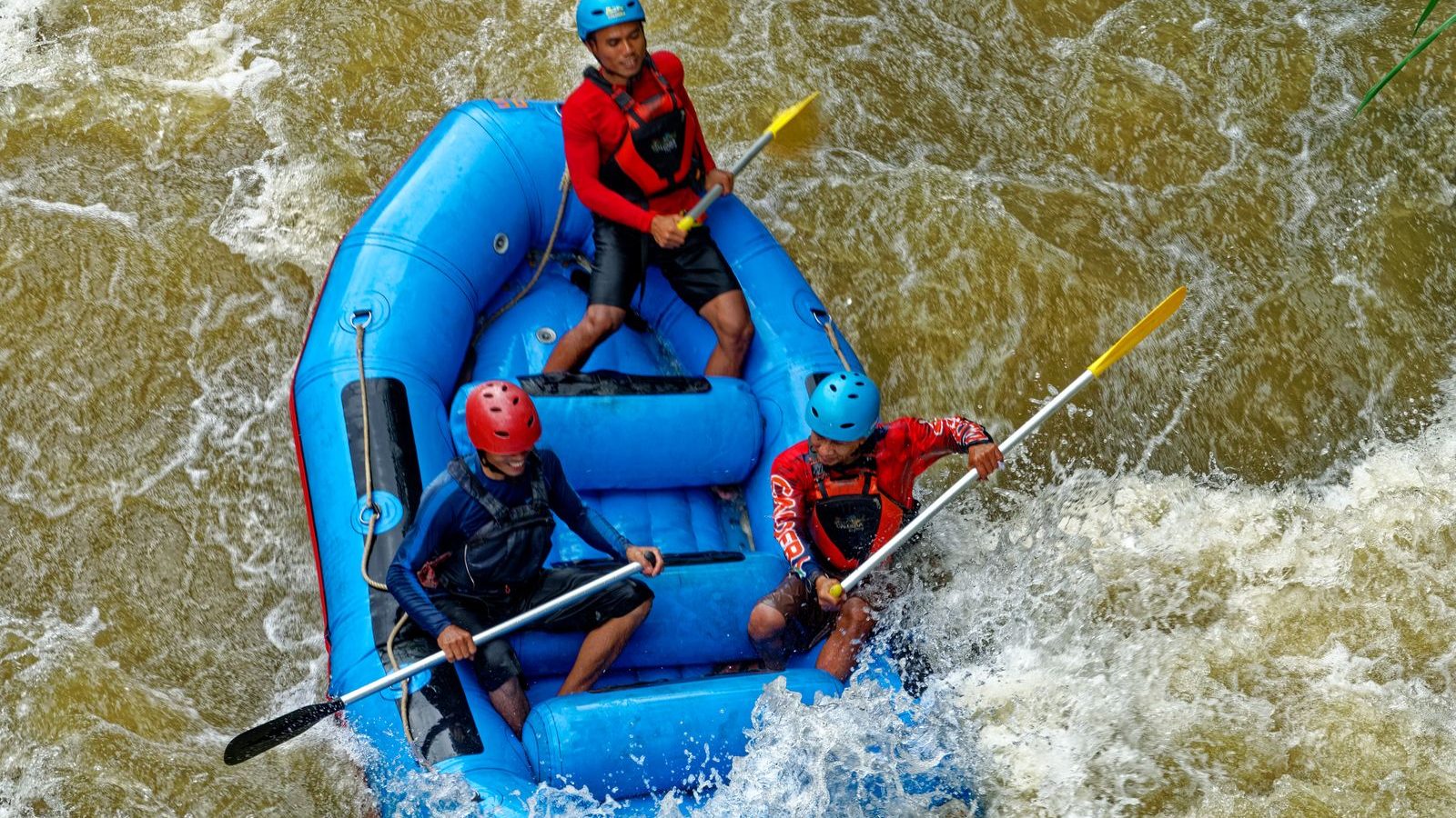 Trois rafteurs casqués pagayant dans un raft gonflable au milieu des rapides, activité rafting en eaux vives