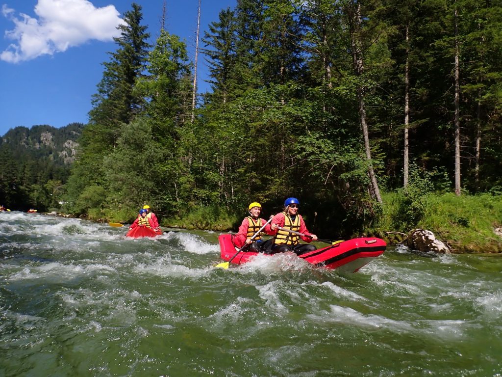 équipage en raft rouge dévalant une rivière de montagne bordée de sapins