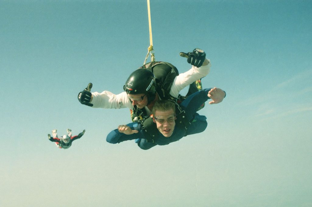 tandem en chute libre avec un second parachutiste visible en arrière-plan, ciel bleu