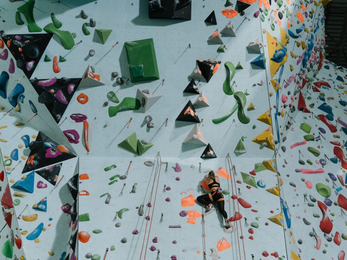 Grimpeuse encordée sur un mur d'escalade en salle aux prises multicolores, ambiance compétition d'escalade en intérieur