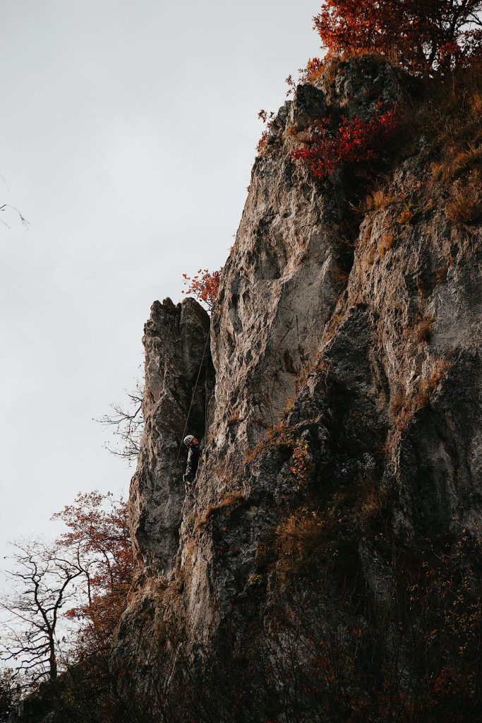 Grimpeur encordé et casqué progressant sur une falaise calcaire en automne, illustration de l'escalade en falaise