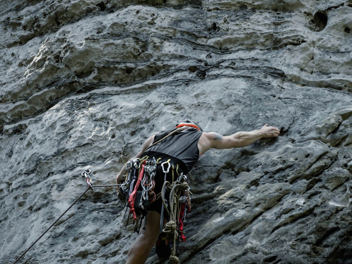 Grimpeur harnaché avec dégaines progressant en tête sur une paroi calcaire verticale, escalade en falaise