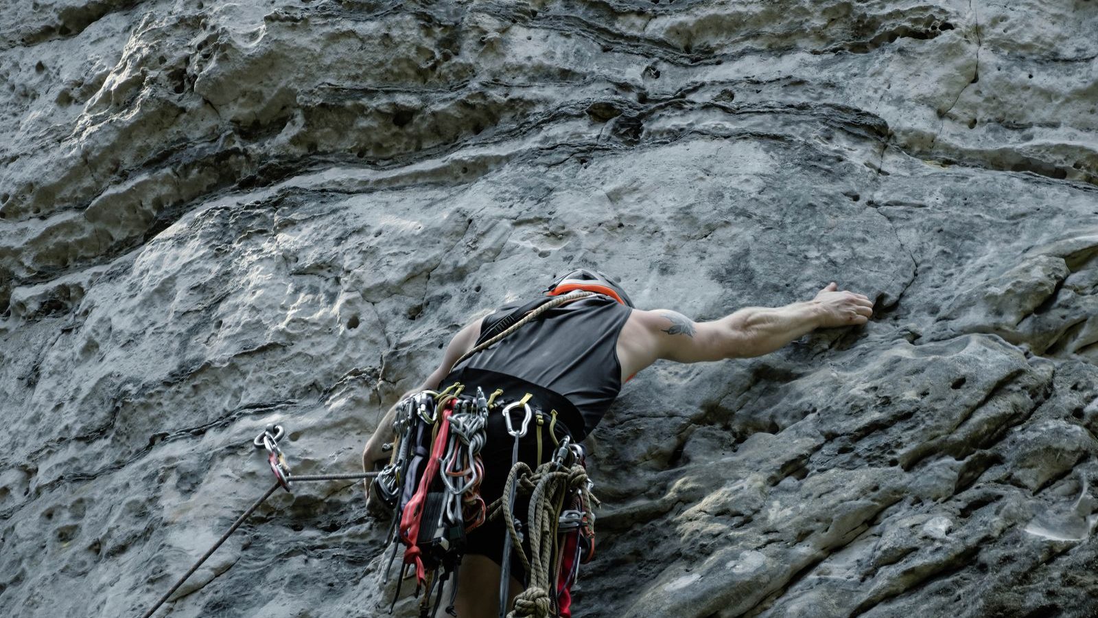 Grimpeur harnaché avec dégaines progressant en tête sur une paroi calcaire verticale, escalade en falaise
