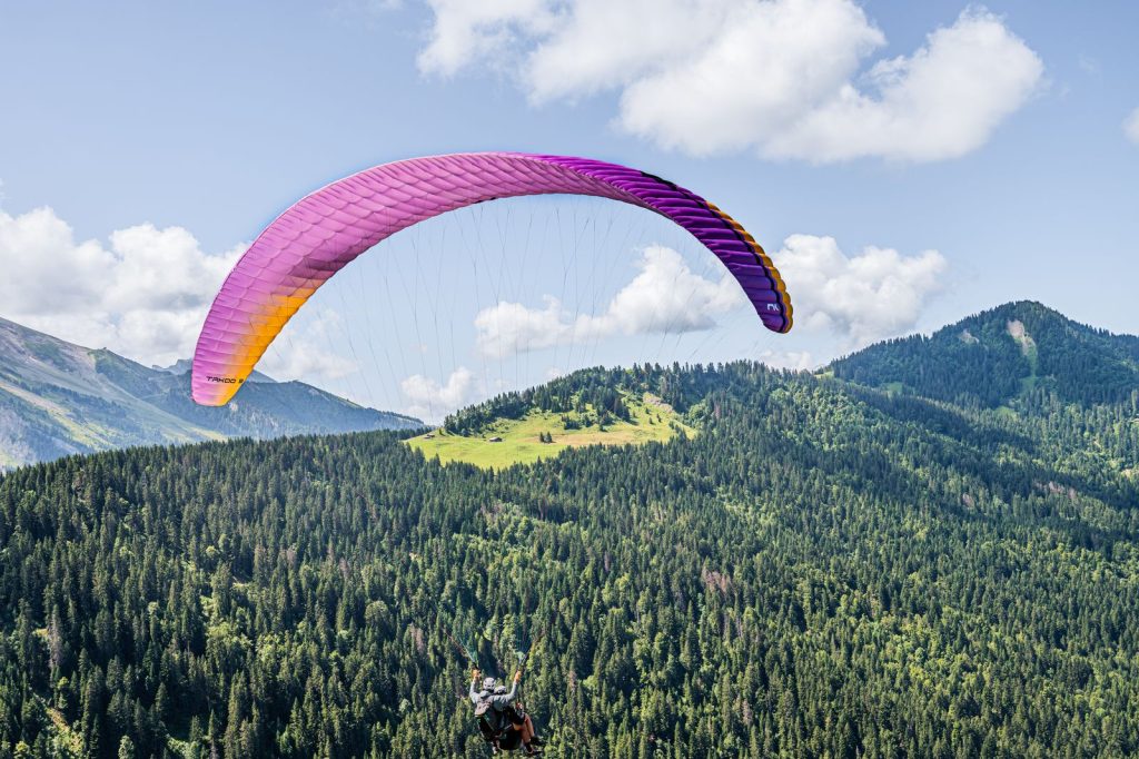 Parapente biplace en vol au-dessus de crêtes boisées et de sommets verdoyants, illustration du parapente au Puy-de-Dôme