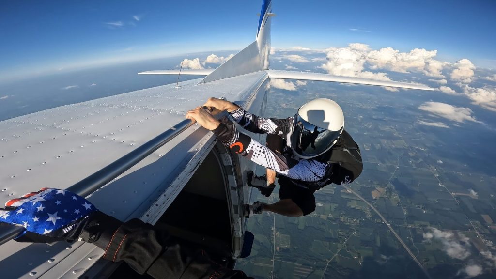 parachutiste casque et visiere miroir, de dos, accroche a l aile de l avion, vue aerienne