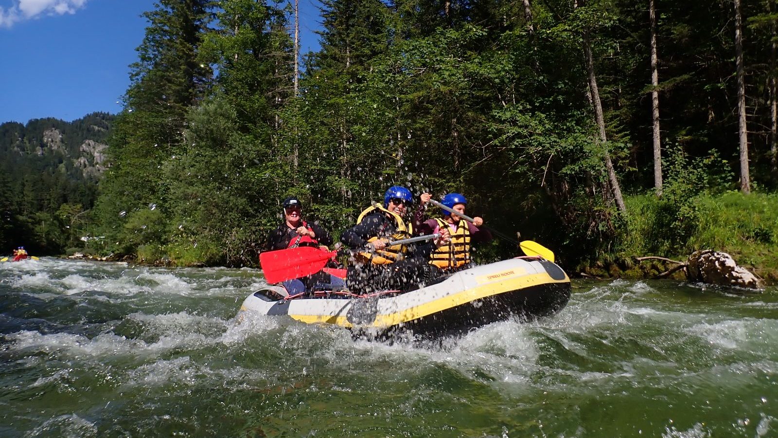 Équipe casquée en raft franchissant des rapides sur une rivière de montagne encaissée entre les sapins, illustrant le rafting engagé sur l'Ubaye