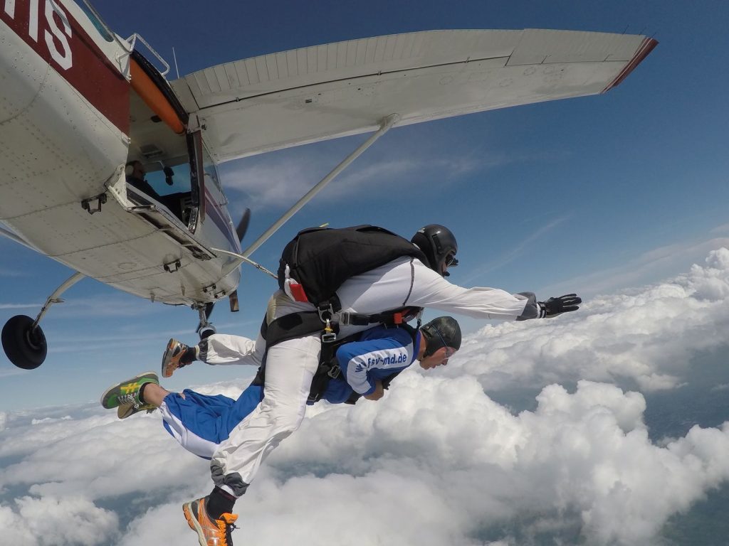 Duo en saut tandem juste après avoir quitté l'avion, au-dessus d'un tapis de nuages, illustrant le saut en parachute encadré