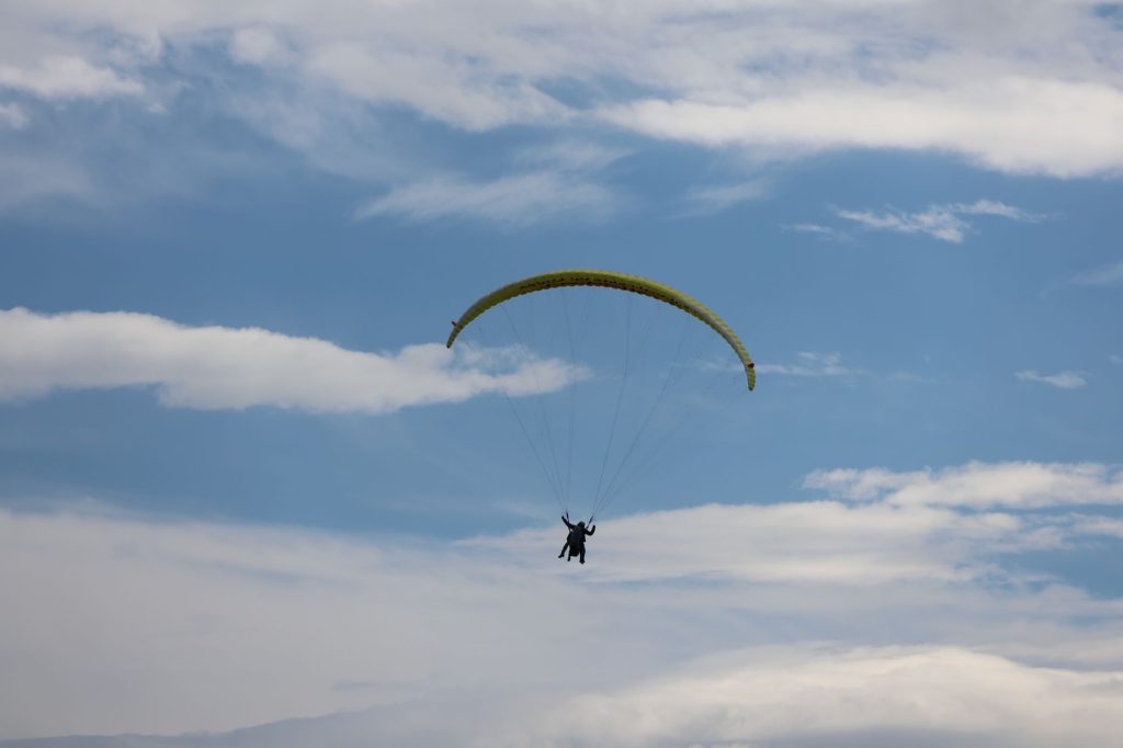 voile de parapente en vol sous un ciel nuageux, silhouette du pilote suspendue au baudrier